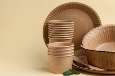 Bej arka planda tek kullanımlık masa takımı ve yeşil yapraklar, yakın plan. Metin için boşluk