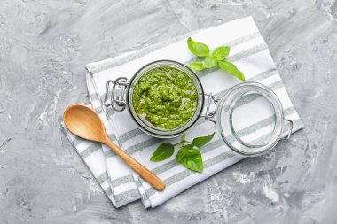 Kavanozda taze pesto sosu, fesleğen yaprakları ve gri desenli masada kaşık, düz yatıyordu.