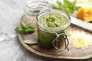 Kavanozda taze pesto sosu, gri desenli masada rende ve malzemeler, yakın plan.
