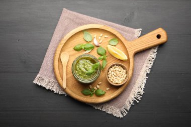 Kavanozda taze pesto sosu, siyah ahşap masada kaşık ve malzemeler.
