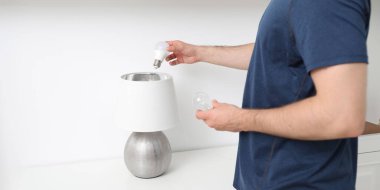 Man changing incandescent light bulb for fluorescent one in lamp indoors, closeup