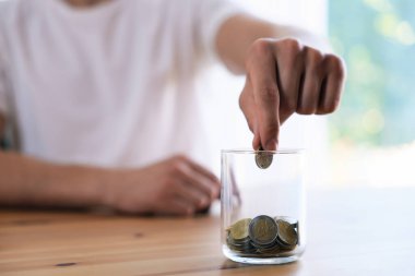Adam parayı kapalı bir masada kavanoza koyuyor, yakın plan.