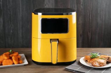 Modern hava kızartma makinesi ve ahşap masada pişmiş yemekler.