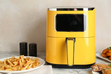 Modern hava kızartma makinesi ve beyaz mermer masada pişmiş yemekler.