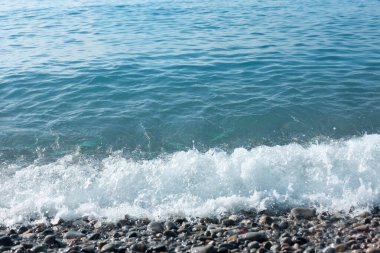 Dalgalı deniz manzarası ve kumsaldaki çakıl taşları.
