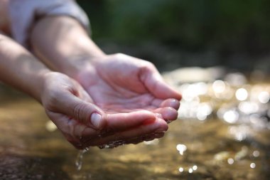 Su kavramını sakla. Nehrin yanında elinde temiz su tutan kadın, yakın plan.