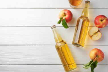 Cam şişelerde nefis elma şarabı ve beyaz ahşap masada elmalar, düz yatak. Metin için boşluk
