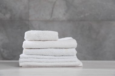 Gri duvara karşı açık ahşap masada katlanmış havlular, yakın plan.