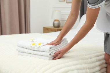 Oda hizmetçisi beyaz havlu ve tesisat çiçeklerini yatağın içine koyuyor, yakın plan.