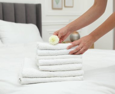 Kapalı alandaki yatakta beyaz havlu yığınına yıldız çiçeği koyan kadın, yakın plan.