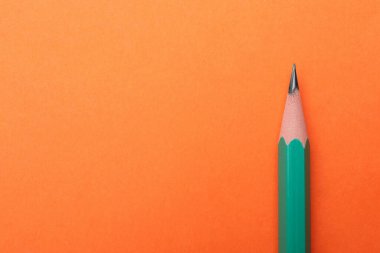 Turuncu arka planda keskin bir grafit kalem, üst manzara. Metin için boşluk