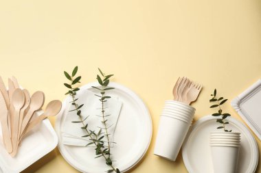 Tek kullanımlık sofra takımı ve okaliptüs dalları bej arka planda, düz yerde. Metin için boşluk