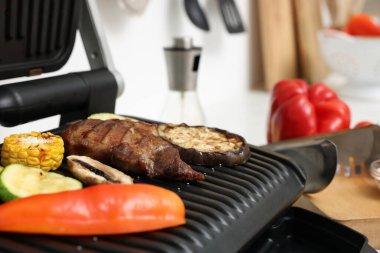 Electric grill with tasty meat and vegetables on table in kitchen, closeup