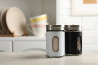 Salt and pepper shakers on light wooden table in kitchen, closeup. Space for text