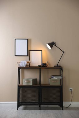 Stylish lamp, other decor and books on console table near beige wall indoors