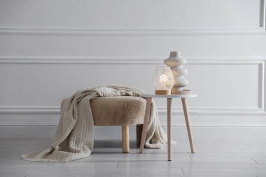 Stylish lamp and vase on white table near pouf indoors