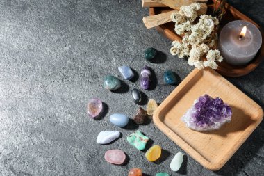 Farklı güzel değerli taşlar, palo santo, mum ve kuru çiçekler gri masada, düz yerde. Metin için boşluk