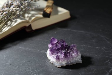 Güzel ametist mücevher, lavanta çiçekleri, palo santo ve siyah masa üzerine kitap, yakın plan.