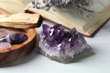 Farklı güzel değerli taşlar, palo santo, beyaz masada kitap ve lavanta çiçekleri, yakın plan.