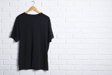 Beyaz tuğla duvara karşı siyah tişörtlü bir askı. Tasarım için model