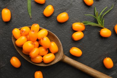 Taze deniz dikenli böğürtlen, kaşık ve yapraklar siyah masada, düz yatar