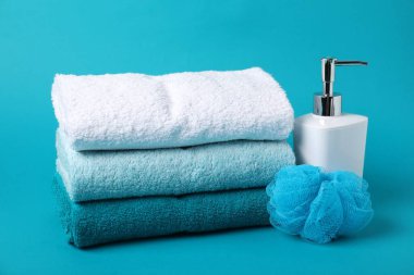 Temiz havlu yığını, kozmetik ürünü ve açık mavi arka planda sünger.