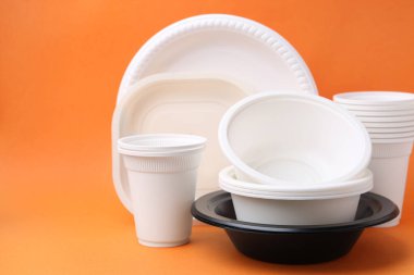 Turuncu arkaplanda tek kullanımlık plastik sofra takımı, yakın plan.