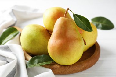 Taze armutlar ve yeşil yapraklar beyaz ahşap masada, yakın plan.