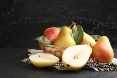 Siyah masadaki hasır kasede taze armut ve yapraklar, yakın plan.