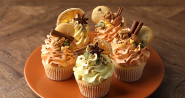 Renkli kremalı lezzetli kekler, baharatlar, kurabiyeler ve fındıklar ahşap masada, yakın plan.