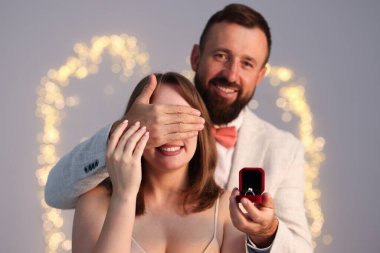 Nişan yüzüklü bir adam, açık gri arka planda, bulanık ışıklı, bokeh efektli kız arkadaşına evlenme teklif ediyor.