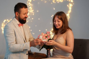 Nişan yüzüklü bir adam, açık gri arka planda, bulanık ışıklı, bokeh efektli kız arkadaşına evlenme teklif ediyor.