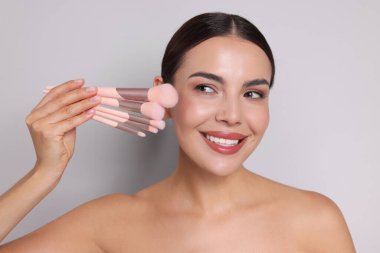 Açık gri arka planda makyaj fırçası olan güzel bir kadın.