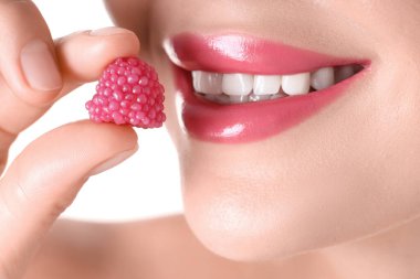 Dudaklarında güzel pembe ruj ve beyaz arka planda ahududu şekeri olan kadın, yakın plan.