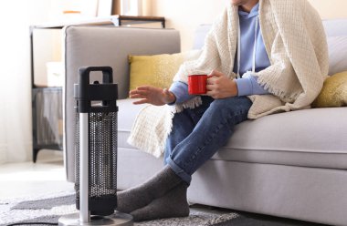 Evinde elektrikli ısıtıcının yanında bir bardak içkisi olan genç adam, yakın çekim.