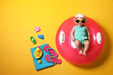 Güneş gözlüklü şirin bir bebek. Şişirilebilir yüzüğü ve sarı arka planda plaj aksesuarları var.