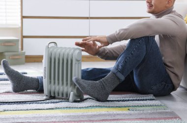 Evdeki elektrikli ısıtıcının yanındaki genç adam, yakın çekim.