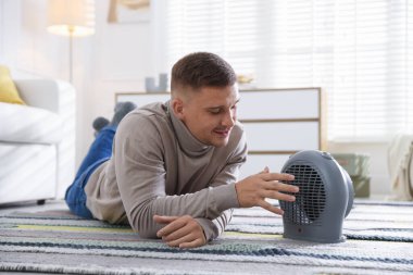 Evdeki elektrikli ısıtıcının yanındaki genç adam.