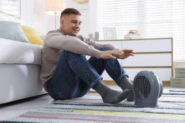 Evdeki elektrikli ısıtıcının yanındaki genç adam.