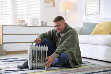 Evdeki elektrikli ısıtıcının yanındaki genç adam.