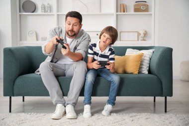 Evde kanepede video oyunu oynayan kontrolörlü baba ve oğul.