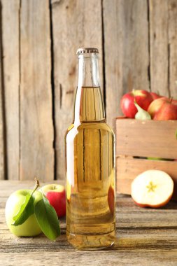 Cam şişede nefis elma şarabı ve tahta masada elmalar.