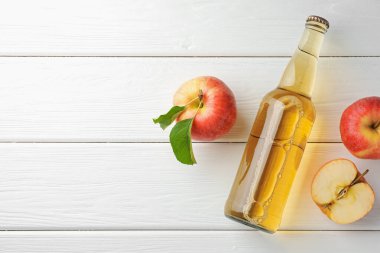 Cam şişede nefis elma şarabı ve beyaz ahşap masada elmalar, düz yatak. Metin için boşluk