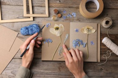 Ahşap masa, üst manzara, kuru çiçekleri deftere koyan kadın.