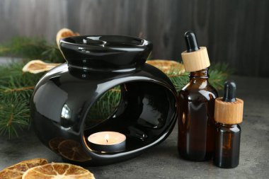 Aroma lambası yanan mum, kuru portakal dilimleri, damlalar ve köknar ağacı dalları gri desenli masa üzerinde ahşap arka planda, yakın plan