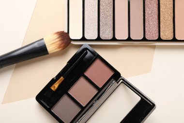 Renkli göz falı paletleri ve bej arka planda makyaj fırçası, düz yatış