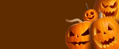 Cadılar Bayramı poster tasarımı. Kahverengi arka plana bakan oyulmuş ürkütücü yüzlü balkabakları. Metin için boşluk