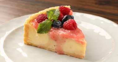 Ahşap masada meyveli ve soslu lezzetli cheesecake yiyen kadın, yakın plan.