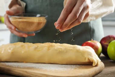 Kadın mutfaktaki çiğ elmalı turtanın üzerine kahverengi şeker serpiyor.