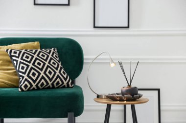 Stylish lamp and reed diffuser on side table near armchair with pillows indoors